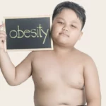 An overweight boy holding a sign that says obesity.