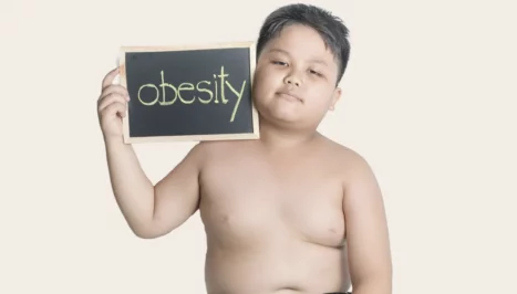 An overweight boy holding a sign that says obesity.