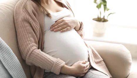 A woman who became pregnant after gastric sleeve surgery sits on a couch.