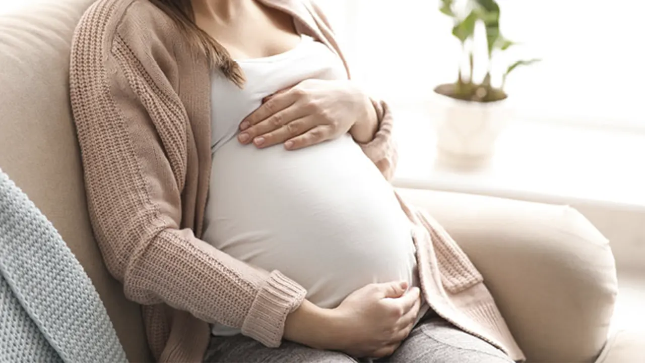 A woman who became pregnant after gastric sleeve surgery sits on a couch.