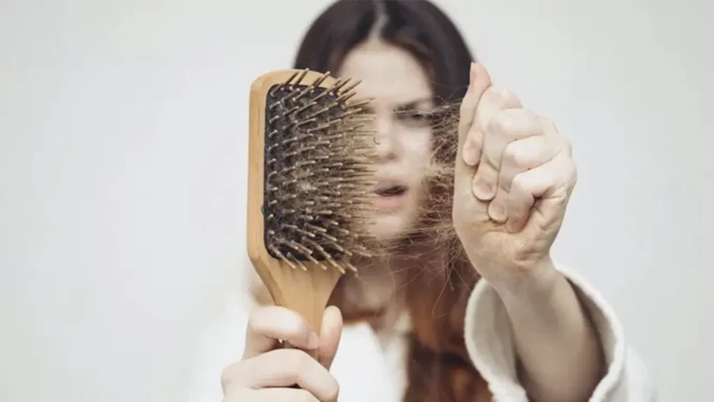 A woman suffering from hair loss removes her hair from her brush.