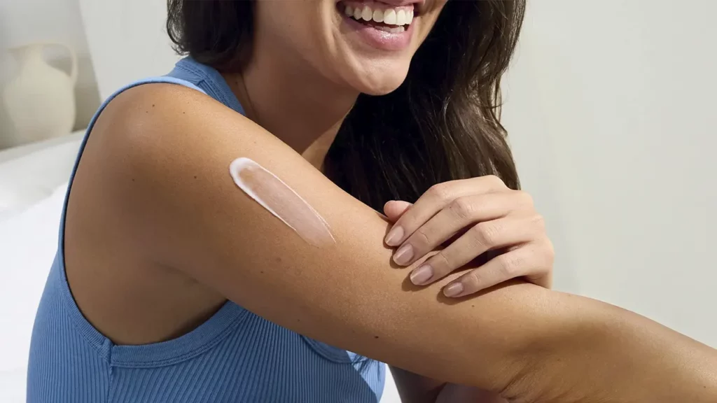 A young woman applying skin care cream to her arm.